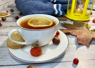 Cozy autumn photo with sweater, cup of tea with lemon and autumn leaves 