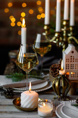 Beautiful table setting for family Christmas dinner at home. Cozy atmosphere, candlelight. Wine glasses, vintage chandelier, elegant interior. Fir tree branches, wooden furniture, dark, bokeh