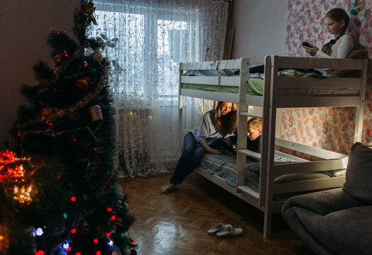 A cozy winter evening with family gathered in a warmly lit bedroom, sharing stories near the Christmas tree