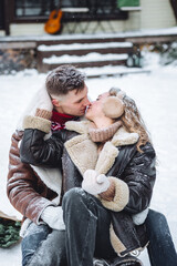 Obraz premium Portrait of pretty cheerful beautiful couple in warm clothes, knitted sweater embracing smiling having fun outdoors in winter in the park. Snowflakes, frosty day, snow all around. Countryside house