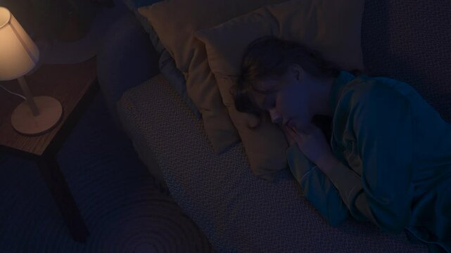 Woman in pajama sleeping in bed in dark apartment room, monster hiding under bed. Girl waking up hearing storm and lightning. Halloween horror concept.