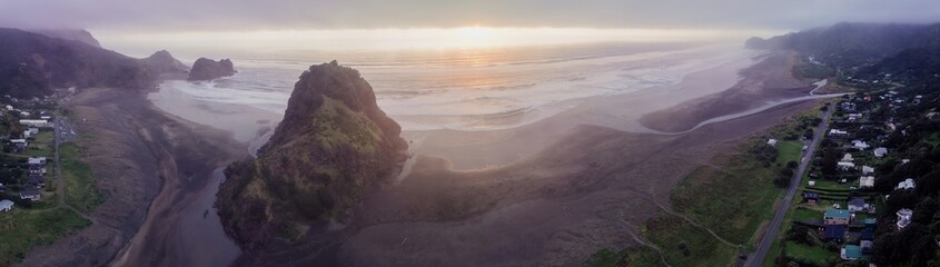 Wild foggy ocean coastline and Lion Rock at sunset in Piha, Auckland, New Zealand.