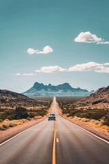 Fototapeta premium An open road stretching through a vast desert with a classic car driving towards distant mountains the landscape is rich with earthy tones and the sky is a brilliant blue with a few scattered clouds