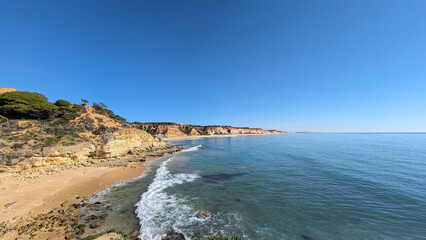 Summer weather on the beaches of the Algarve in Portugal with breaking waves, wet rocks in the sand and overgrown slopes on the coast