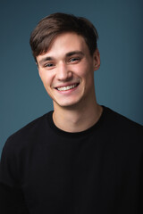A guy of model appearance in black clothes poses on a studio background. Male fashion portrait
