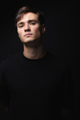 Obraz premium A guy of model appearance in black clothes poses on a black studio background. Male fashion portrait