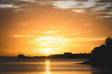 Naklejka premium sunset over the sea with a city silhouette