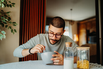Young caucasian man eating corn flakes for breakfast at home