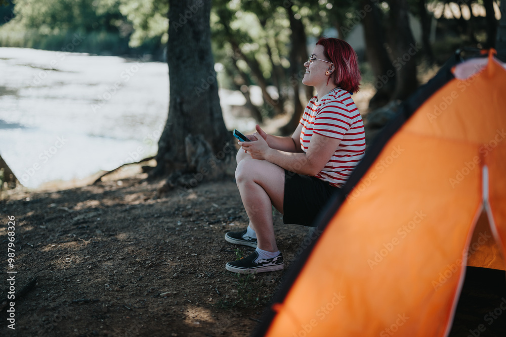 Wall mural young woman relaxing by the lake on a camping trip, enjoying nature and serenity.