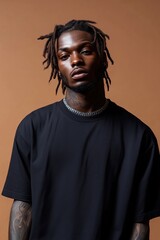 Fototapeta premium Young Black man with dreadlocks wearing a black shirt poses against a brown backdrop.
