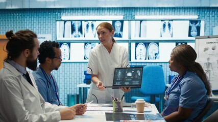 Diverse medical team examining test results and discussing innovative treatment plans at a modern clinic to enhance patient care quality. Doctors and nurses review x ray scans. Camera B.