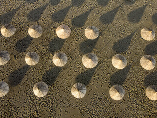 Parasols on a sandy beach by the sea, drone shot. Cane parasols on the seashore.