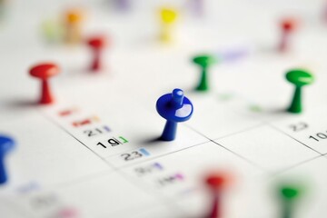 Fototapeta premium Close-up of a colorful calendar with vibrant pushpins, focusing on a blue pin symbolizing a highlighted event, while scattered red, green, yellow, and purple pins represent other important dates and e