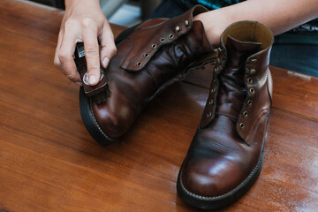 Close up of a hands polishing a leather boots with brush, on wooden table, shoes shining and cleaning.