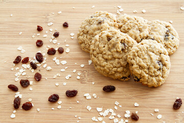 Freshly baked homemade oatmeal raisin cookies on a wooden cutting board.  Ingredients sprinkled around cookies