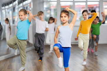 Fototapeta premium Active preteen girl practicing sport dances with other children and teacher during dancing classes