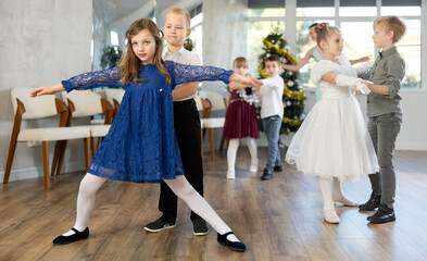 Couple of smiling tweens, boy and girl in festive clothing performing graceful waltz with group...