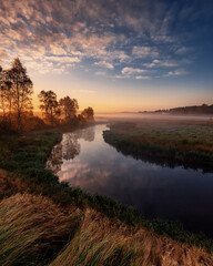 Fototapeta premium Scenic river flowing through misty landscape at sunrise