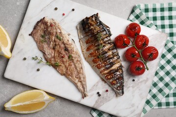 Board with delicious grilled mackerel, tomatoes, spices and lemon on grey table, flat lay