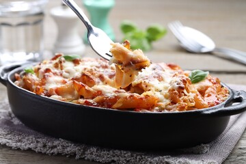 Eating delicious al forno pasta at wooden table, closeup