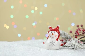 Cute snowman and other Christmas decor against beige background with blurred lights, bokeh effect. Space for text