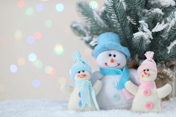 Cute snowmen and fir branches against beige background with blurred lights, bokeh effect. Space for text
