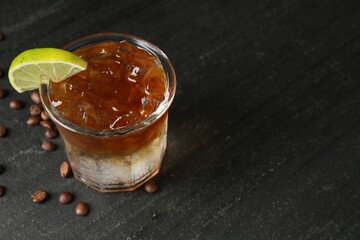 Refreshing espresso tonic drink with slice of lime and coffee beans on dark table, closeup. Space...