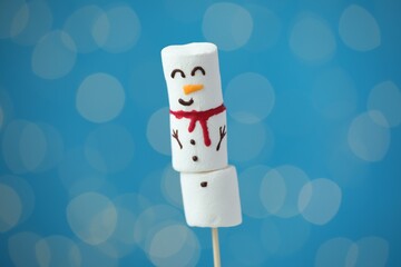 Funny snowman made of marshmallows on blue background with blurred lights