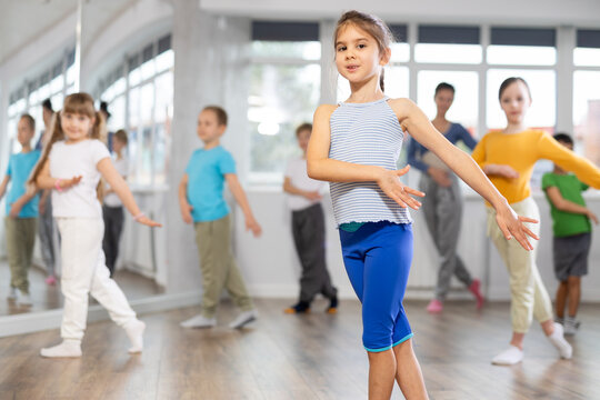 Children studying modern style dances with female teacher in dance class indoors