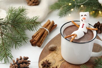 Funny snowman made with marshmallows in cup of hot chocolate and winter decor on white table