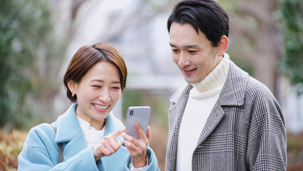 スマホを見る夫婦（冬服・コート・上着）