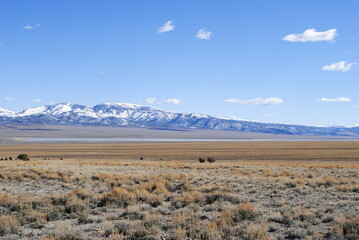 Snow-covered mountains rising up in the distance over vast high mountain desert landscape on a sunny winter day