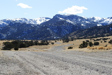 Dirt road leading through the desert valley with beautiful snow capped mountains in the distance
