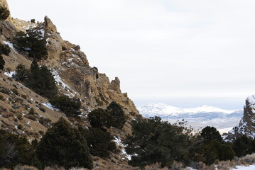 Rocky cliff mountainside with even larger snowy mountains in the distance on a cloudy winter day
