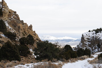 Rocky cliff mountainside with even larger snowy mountains in the distance on a cloudy winter day