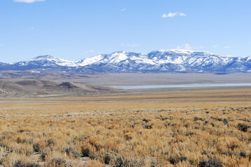 Snow-covered mountains rising up in the distance over vast high mountain desert landscape on a sunny winter day