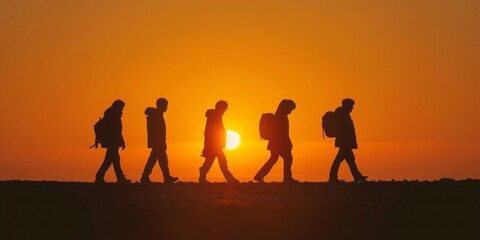 Fototapeta premium A group of hikers walking in a line, silhouetted against an orange sunset sky