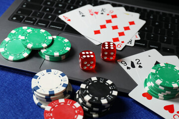 Poker chips, laptop, playing cards and dices on blue table. Online game