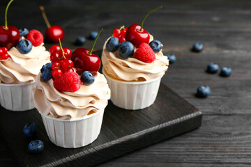 Tasty cupcakes with different berries on black wooden table, closeup
