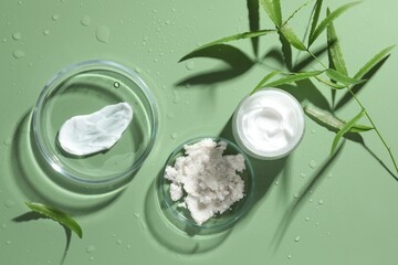 Fototapeta premium Petri dishes with cosmetic products and leaves on green background, flat lay