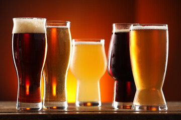 Glasses with different types of beer and snacks on wooden table against color background, closeup