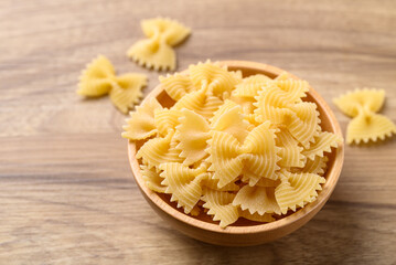 Uncooked farfalle pasta (bow tie shape) in wooden bowl, Italian food ingredient
