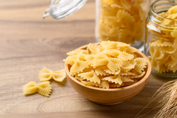 Uncooked farfalle pasta (bow tie shape) in wooden bowl and glass jar, Italian food ingredient