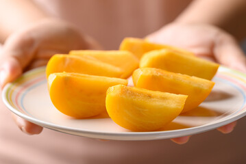 Sliced ripe persimmon fruit on plate holding by hand, Healthy eating