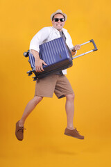 Asian Traveller Man Wear Hat and Sunglasses Jumping While Holding Suitcas Isolated on Yellow Background