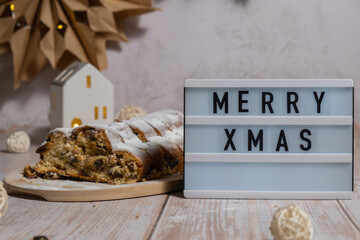 Lightbox with saying MERRY XMAS. Traditional German Christmas stollen cake in background of handmade festive decor. Winter holiday treats. Vegan baking recipe preparation