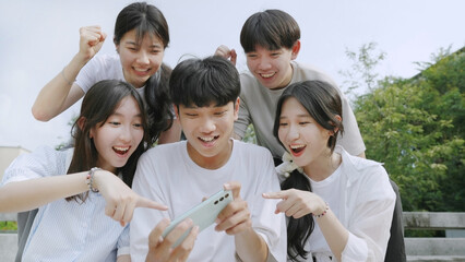 Happy young group of friends using phone and smiling together outdoor.