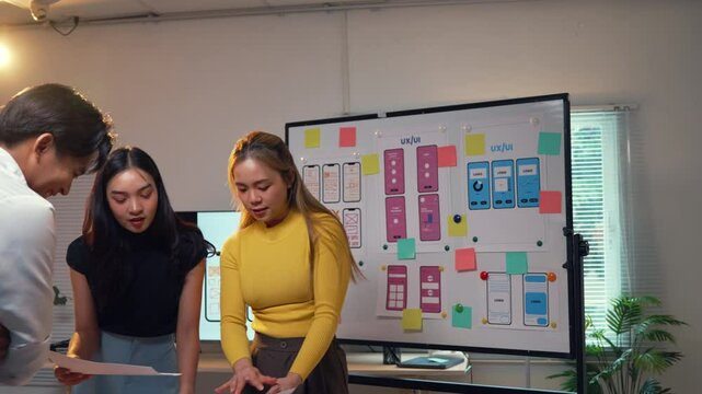 Asian uiux designers collaborate in an office setting, focusing on a mobile application project. The team engages in discussions about wireframe prototypes and design strategies