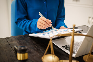 An Asian female lawyer sits at her desk in the office,working on legal documents with computer,providing online legal consulting,reviewing contracts,drafting wills,offering signature certification