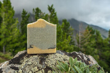Piece of craft soap on the background of mountains, forests and sky. Concept of the image of organic cosmetics in a natural environment